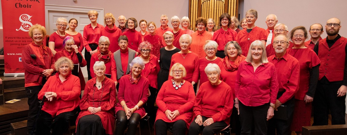 Image of choir dressed in red in front of a historic organ in St Cecilia's Hall