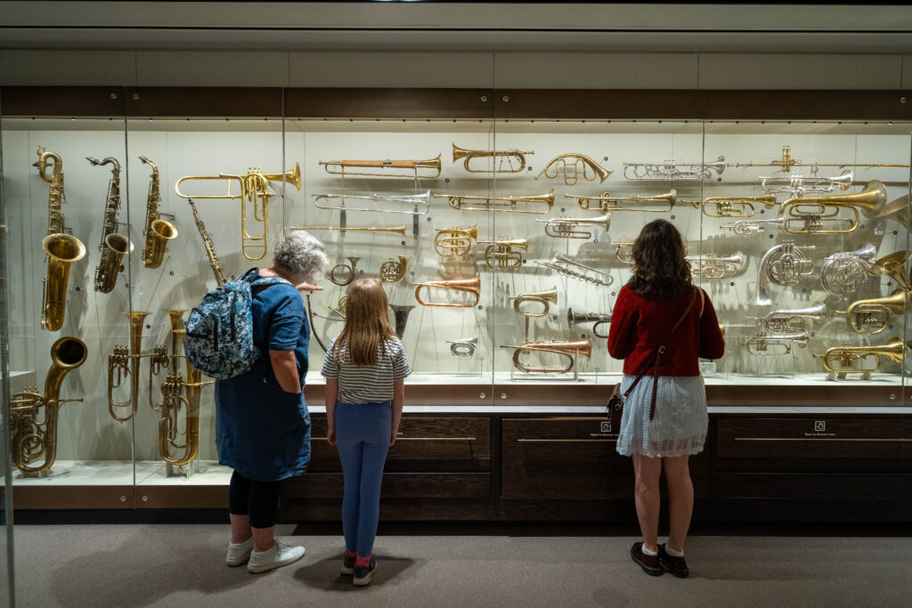 A gallery at St Cecilia's Hall with three people standing in front of display case full of brass instruments